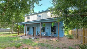 A two-story house with a covered porch, a fenced yard, and a wooden fence in the background. - Blue Heron - New Modern Home in Carrabelle (Carrabelle)