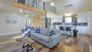 A spacious living area with a grey sofa, wooden coffee table, and a mezzanine with a balcony. - Blue Heron - New Modern Home in Carrabelle (Carrabelle)