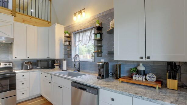 A modern kitchen with white cabinets, a stainless steel dishwasher, a coffee maker, and a knife block. - Blue Heron - New Modern Home in Carrabelle (Carrabelle)