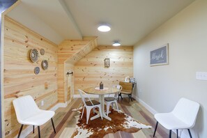 Ein Zimmer mit einer Holzwand, einem runden Tisch mit Stühlen, einem Kuhfellteppich und einem gerahmten Schild an der Wand.