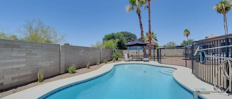 A swimming pool with a brick wall, palm trees, and a covered seating area.
