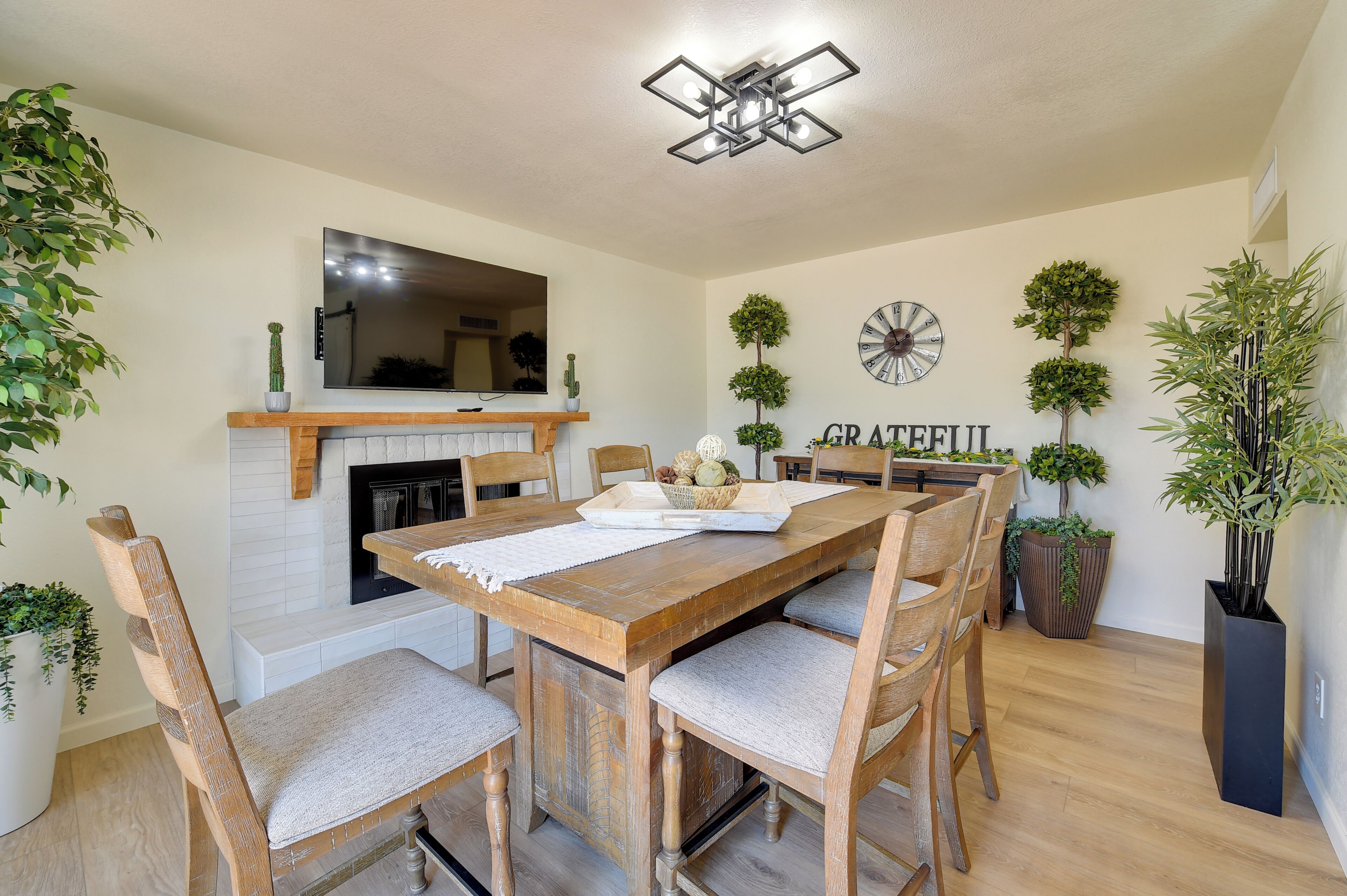 A dining area with a wooden table, chairs, a fireplace, and decorative plants.