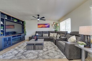 A modern living room with a sectional sofa, a flat-screen TV, a ceiling fan, and a decorative plant. - Private Pool Retreat Near Tucson Attractions (Tucson)