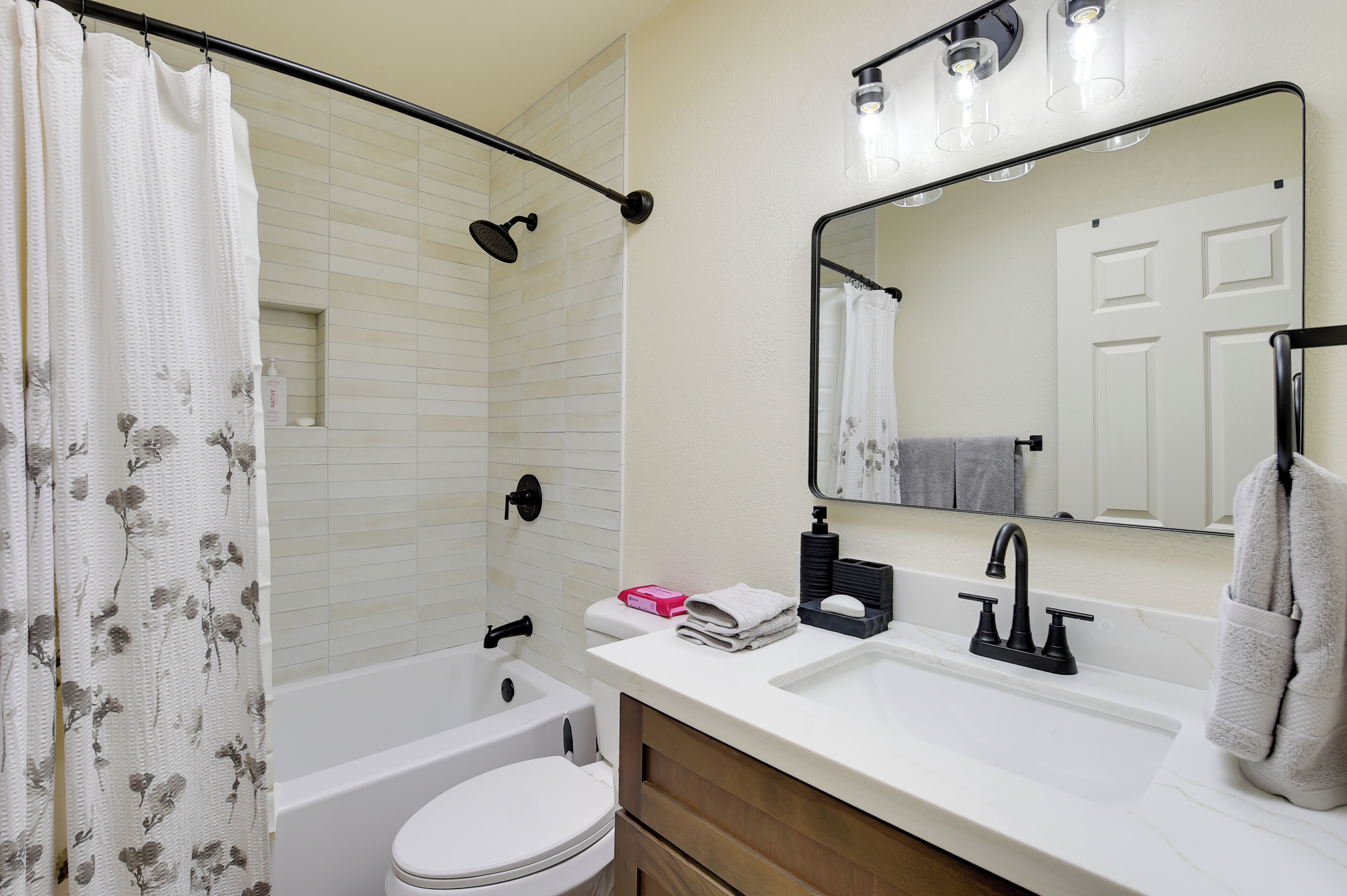 A bathroom with a bathtub, toilet, sink, and a mirror with lights.