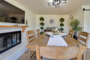 A dining room with a fireplace, wooden table, chairs, and decorative plants. - Pool, Hot Tub, Outdoor Kitchen, Near I10 (Tucson)