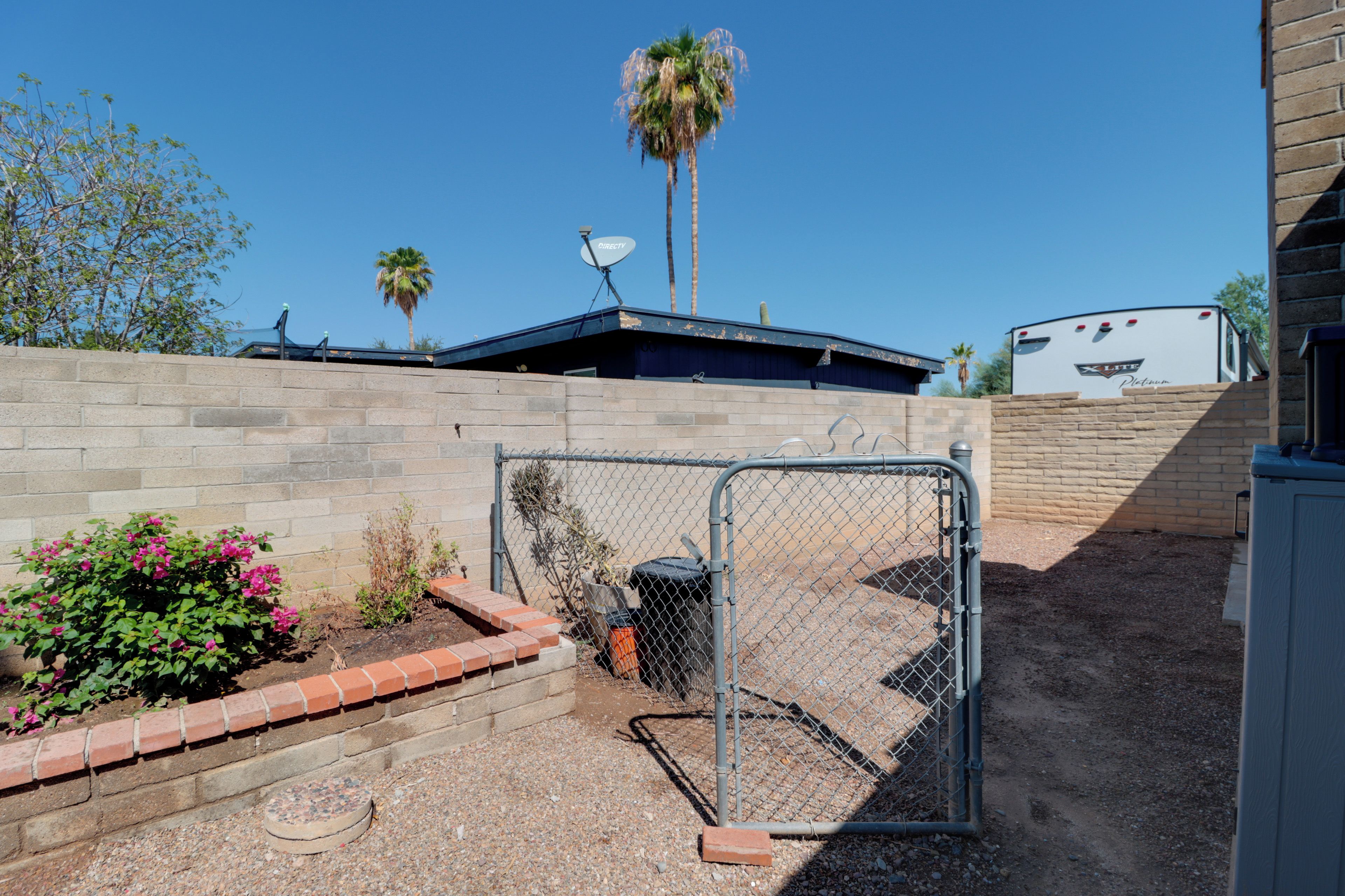 A fenced outdoor area with a brick wall, a satellite dish, and a trailer in the background.