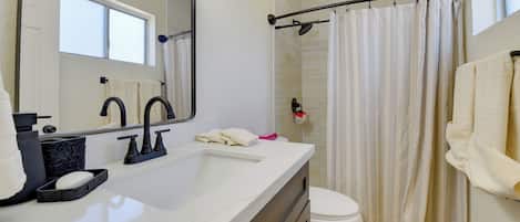 Une salle de bain avec un lavabo blanc, un miroir, des toilettes et un rideau de douche.