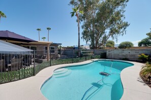A swimming pool with a curved edge, surrounded by a fence and a patio area with outdoor furniture. - Pool, Hot Tub, Outdoor Kitchen, Near I10 (Tucson)