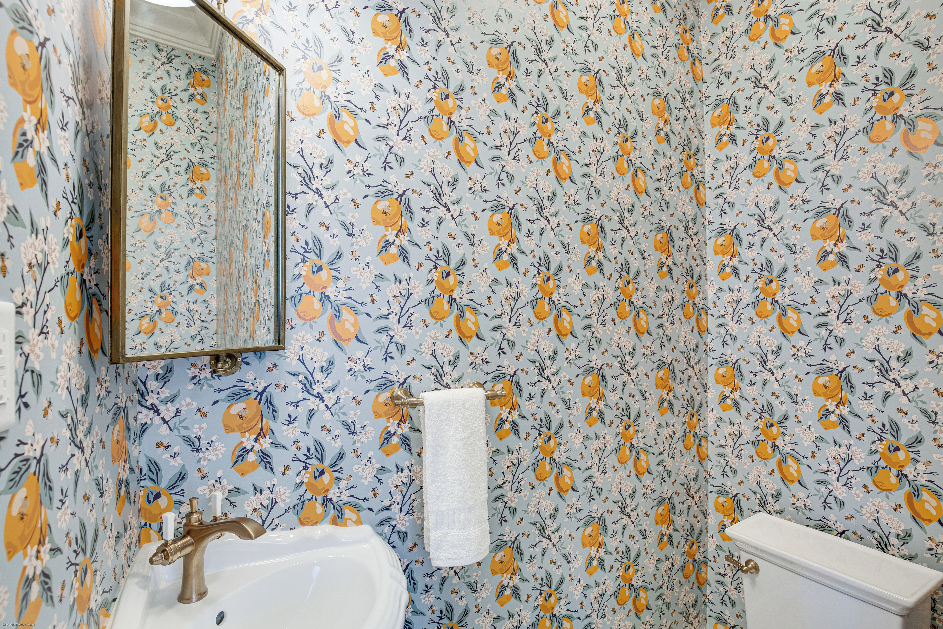 Un baño con papel tapiz floral, un lavamanos, un espejo y un inodoro.