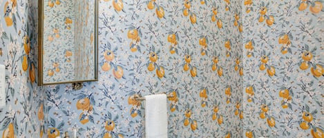 Un baño con papel tapiz floral, un lavamanos, un espejo y un inodoro.