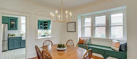 A dining room with a wooden table and chairs, a chandelier, and a view of the outside through large windows.