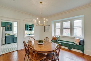 Ein Esszimmer mit Holztisch und Stühlen, einer Chandelierleuchtre und Blick ins Freie durch große Fenster.
