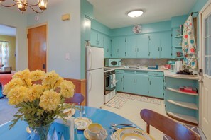 Eine Küche mit türkisfarbenen Schränken, einem weißen Kühlschrank und einem Essbereich mit blauem Tisch und gelben Blumen.