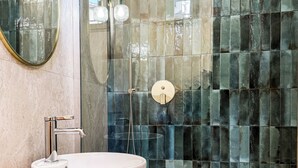 A modern bathroom with a large white sink, a glass-enclosed shower with a handheld showerhead, and a wall with a mosaic tile design. - Bella Vigna (Florence)