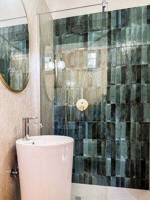 A modern bathroom with a large white sink, a glass-enclosed shower with a handheld showerhead, and a wall with a mosaic tile design. - Bella Vigna (Florence)