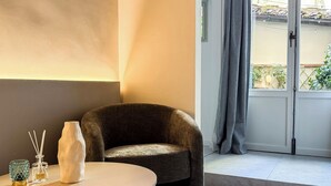 A modern living room with a curved white table, a dark armchair, and a view of a balcony with a door and curtains. - Bella Vigna (Florence)