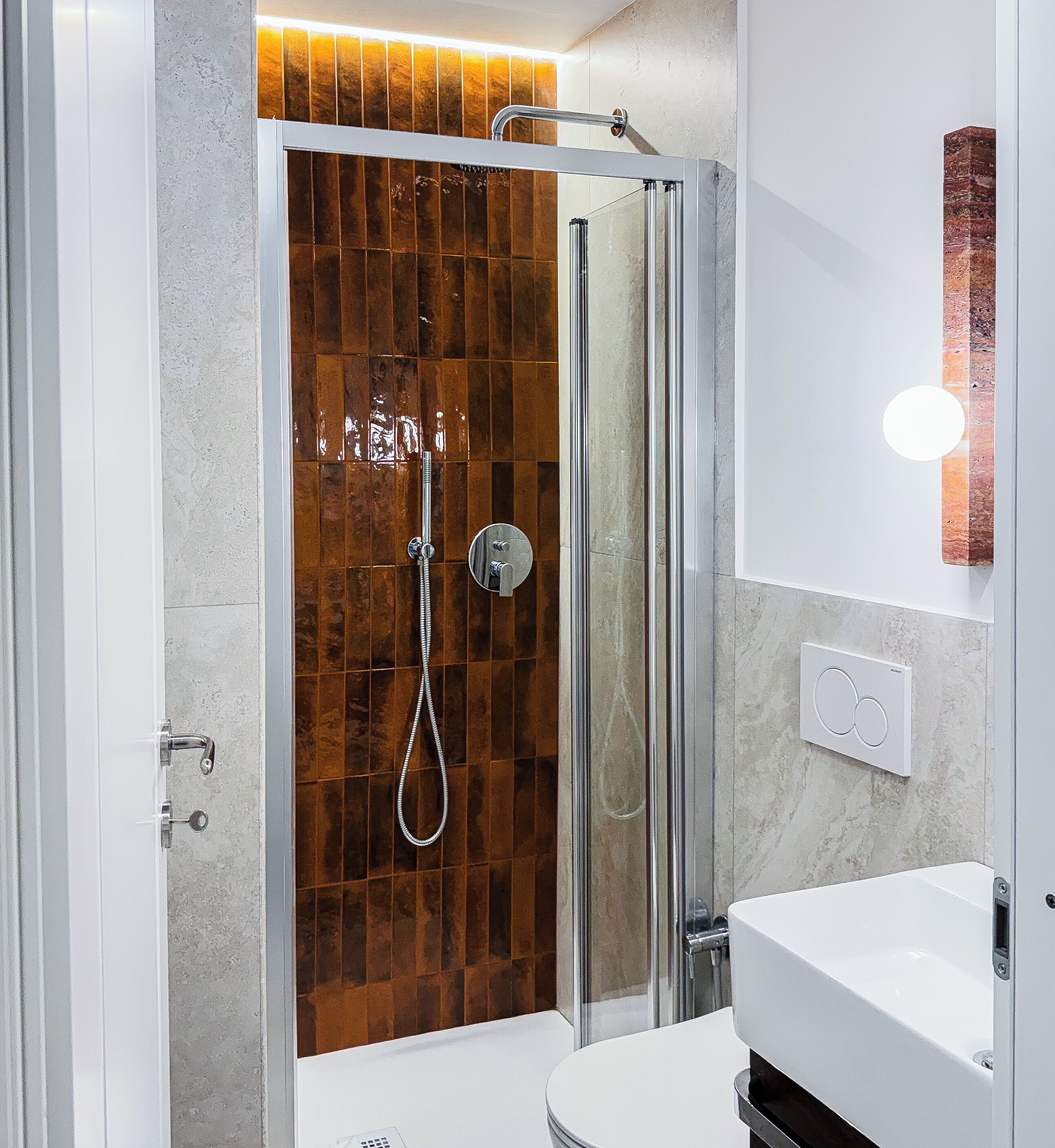 Ein modernes Badezimmer mit einer gläsernen Duschkabine, einem weißen Waschbecken und einer Duschwand mit Marmorfliesen.