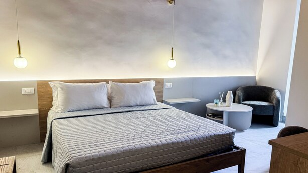A modern hotel room with a large bed, bedside tables, a chair, and a round table. - Bella Vigna (Florence)