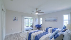 Ein Schlafzimmer mit zwei Betten, einem Deckenventilator und Blick durch eine Schiebetür.