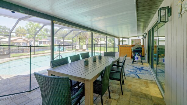 Ein überdachter Patio-Bereich mit Tisch und Stühlen, ein Pool im Hintergrund und Blick auf die umliegende Nachbarschaft.