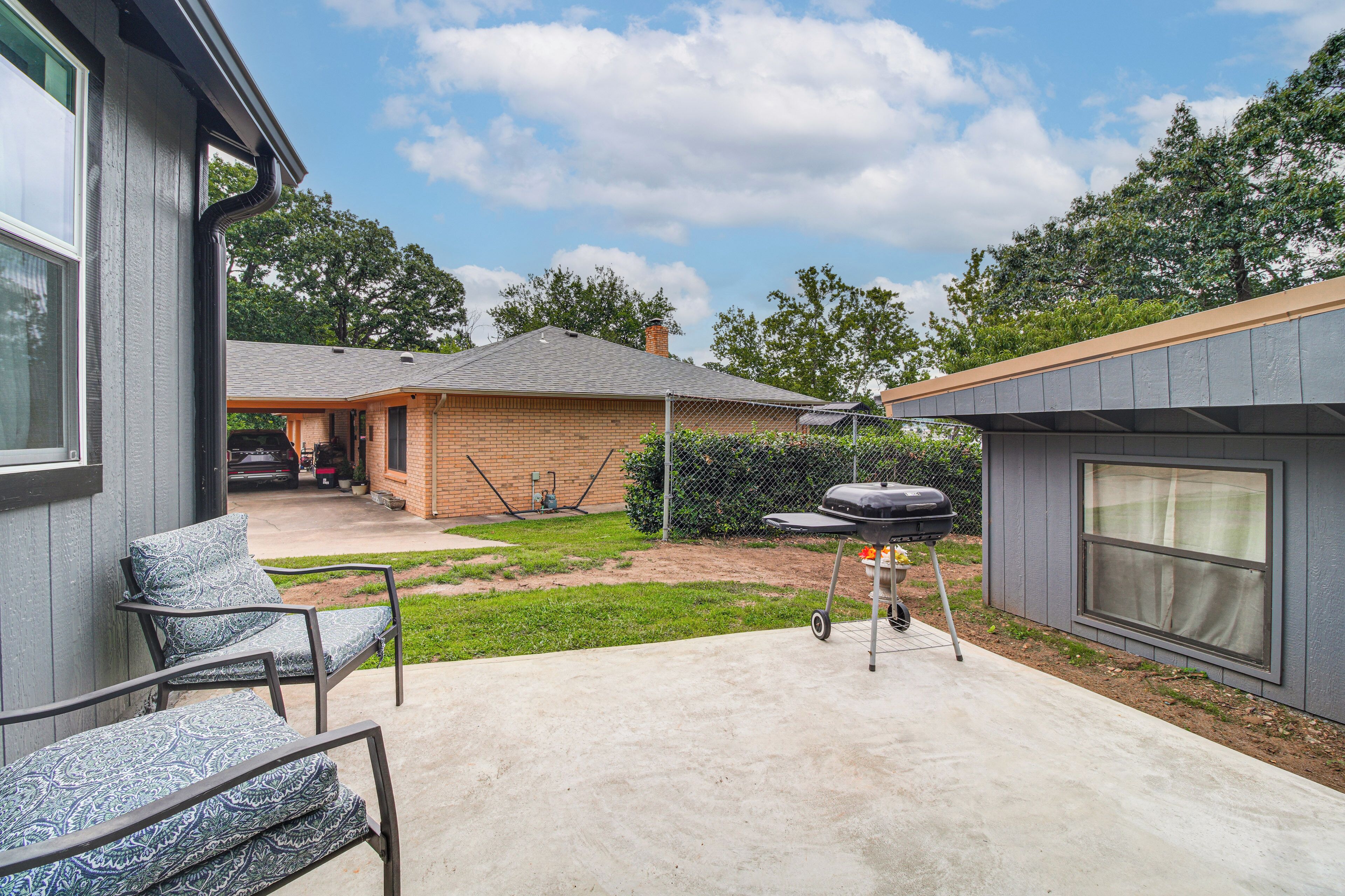 A backyard with a patio, a barbecue grill, a covered outdoor seating area, and a brick building.