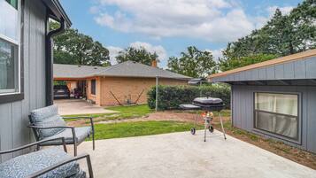 A backyard with a patio, a barbecue grill, a covered outdoor seating area, and a brick building.