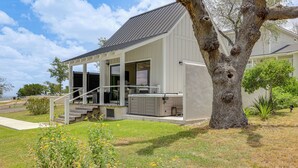 A modern house with a covered porch, a large tree, and a well-maintained lawn. - Hot Tub & Fire Pit! Texas Wine Country Retreat (Fredericksburg)