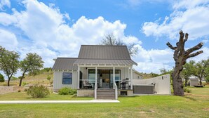 A modern two-story house with a covered porch, large windows, and a well-maintained lawn. - Hot Tub & Fire Pit! Texas Wine Country Retreat (Fredericksburg)