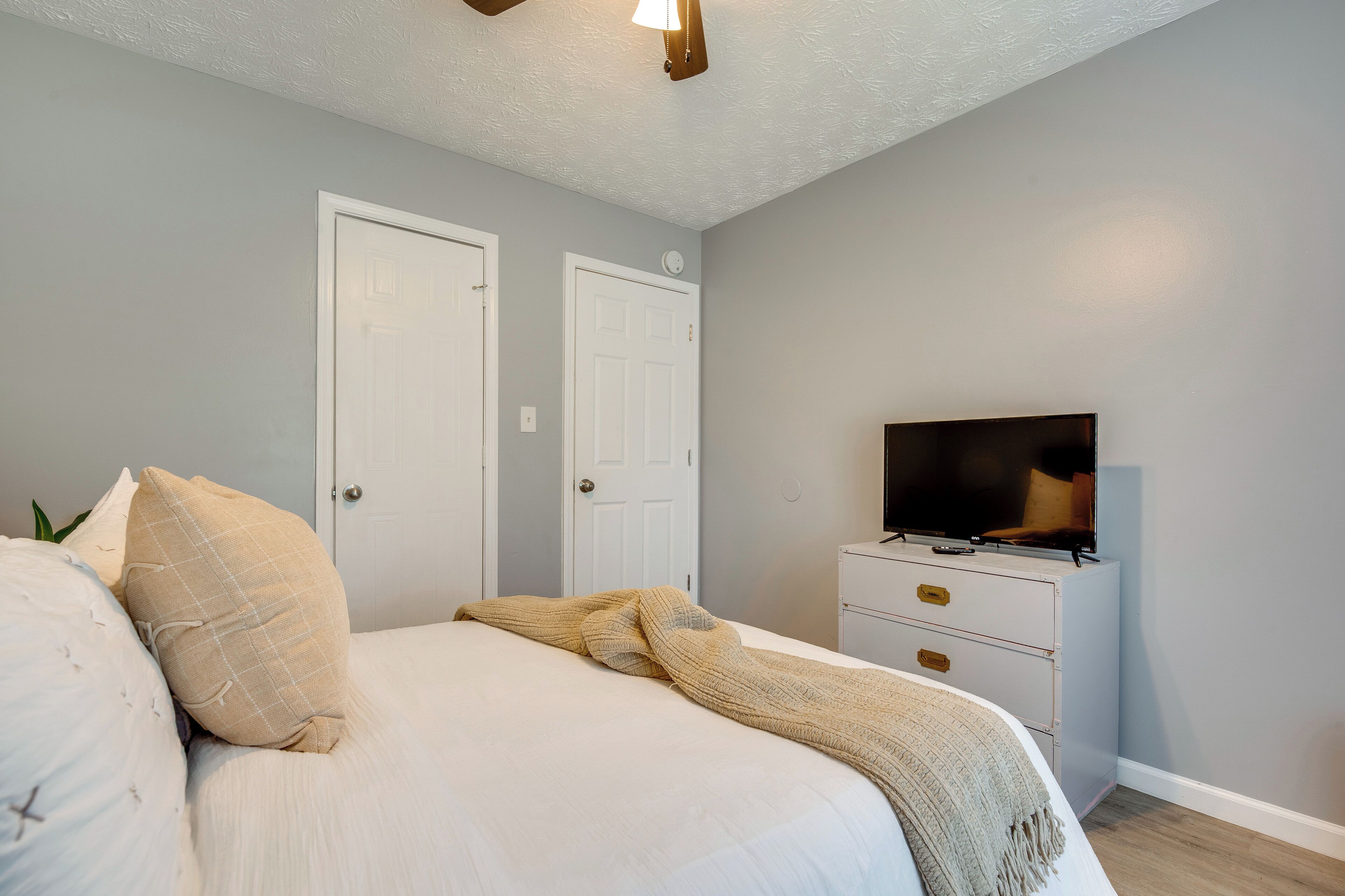 Une chambre à coucher avec un lit, deux portes, un téléviseur posé sur une commode et un luminaire au plafond.