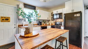 Een moderne keuken met witte kasten, een houten eiland, een zwarte koelkast en een bordje met de waarschuwing om pluizige honden niet aan te raken.