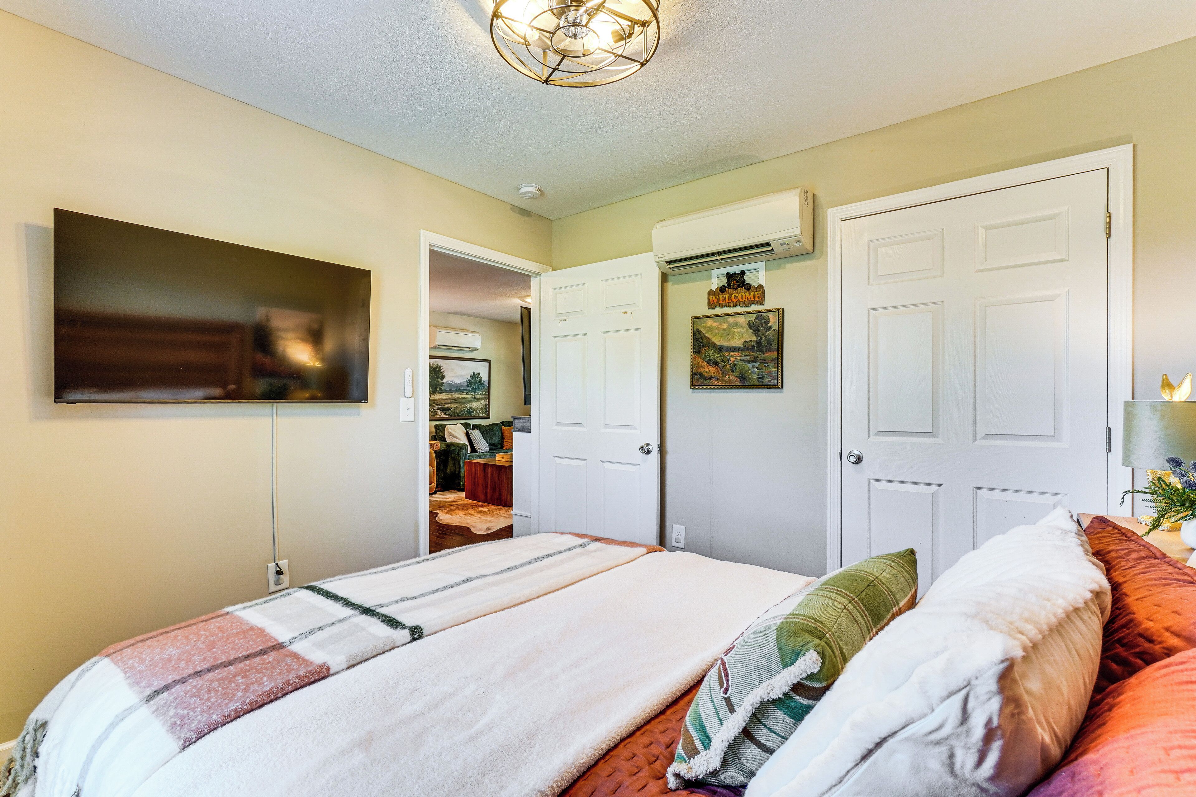 A bedroom with a bed, a TV mounted on the wall, and a door leading to another room.