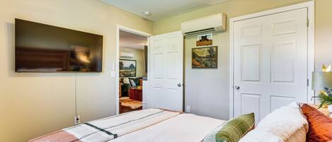 A bedroom with a bed, a TV mounted on the wall, and a door leading to another room.