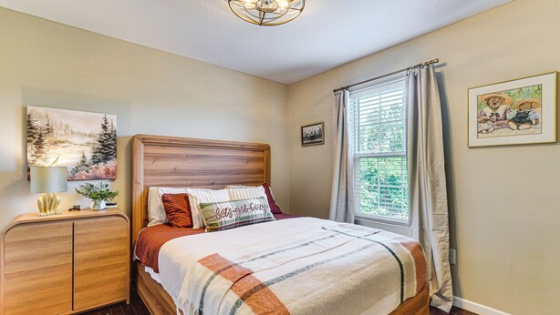 Een slaapkamer met een houten bed, een nachtkastje, een lamp en een raam met gordijnen.