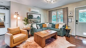 Een woonkamer met een leren fauteuil, een groene bank, een houten salontafel en een schilderij aan de muur.