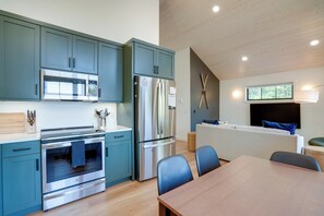 A modern kitchen with stainless steel appliances, teal cabinetry, and a dining area with a wooden table and chairs.