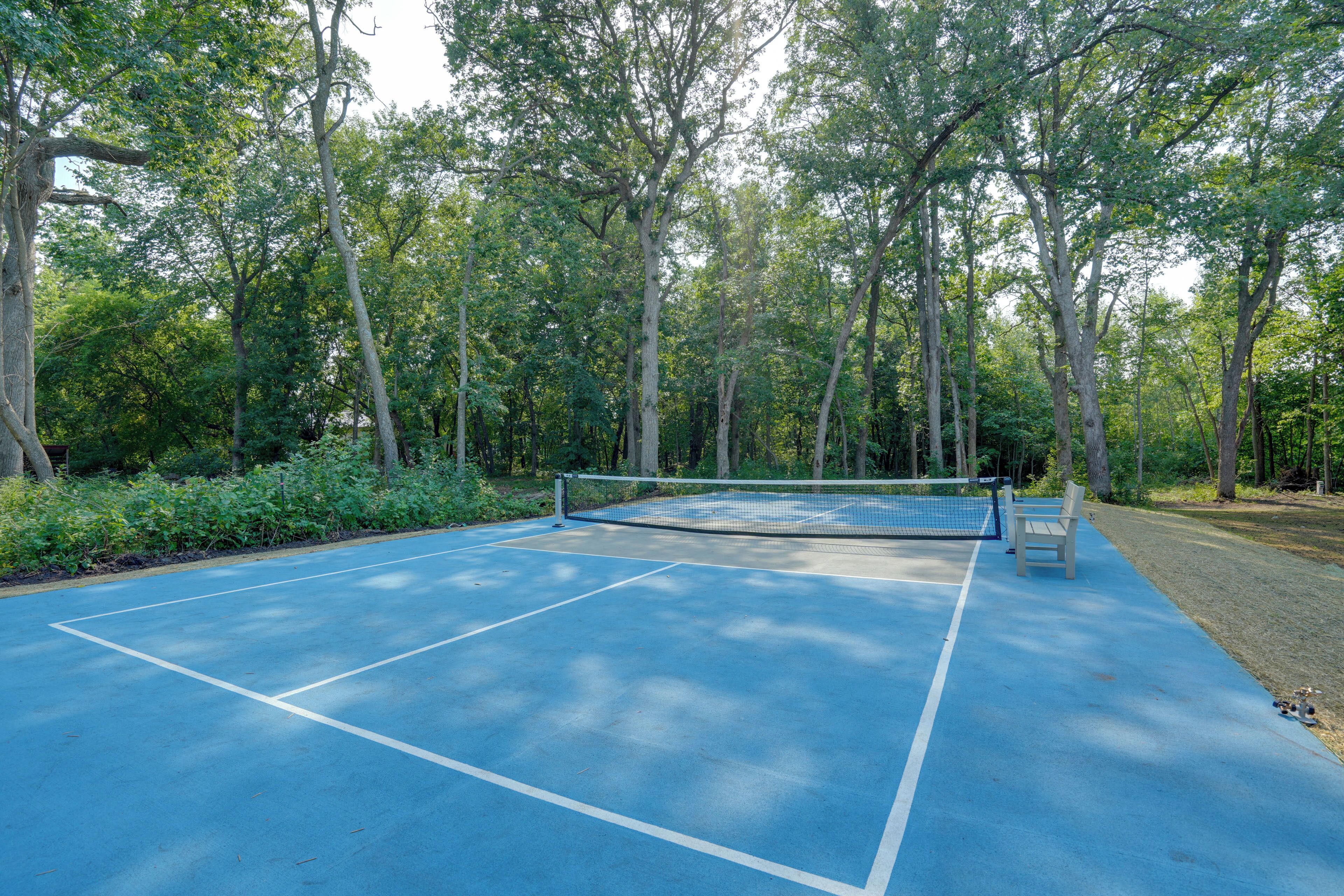 Un court de tennis avec un filet, entouré d’arbres et agrémenté d’un banc.