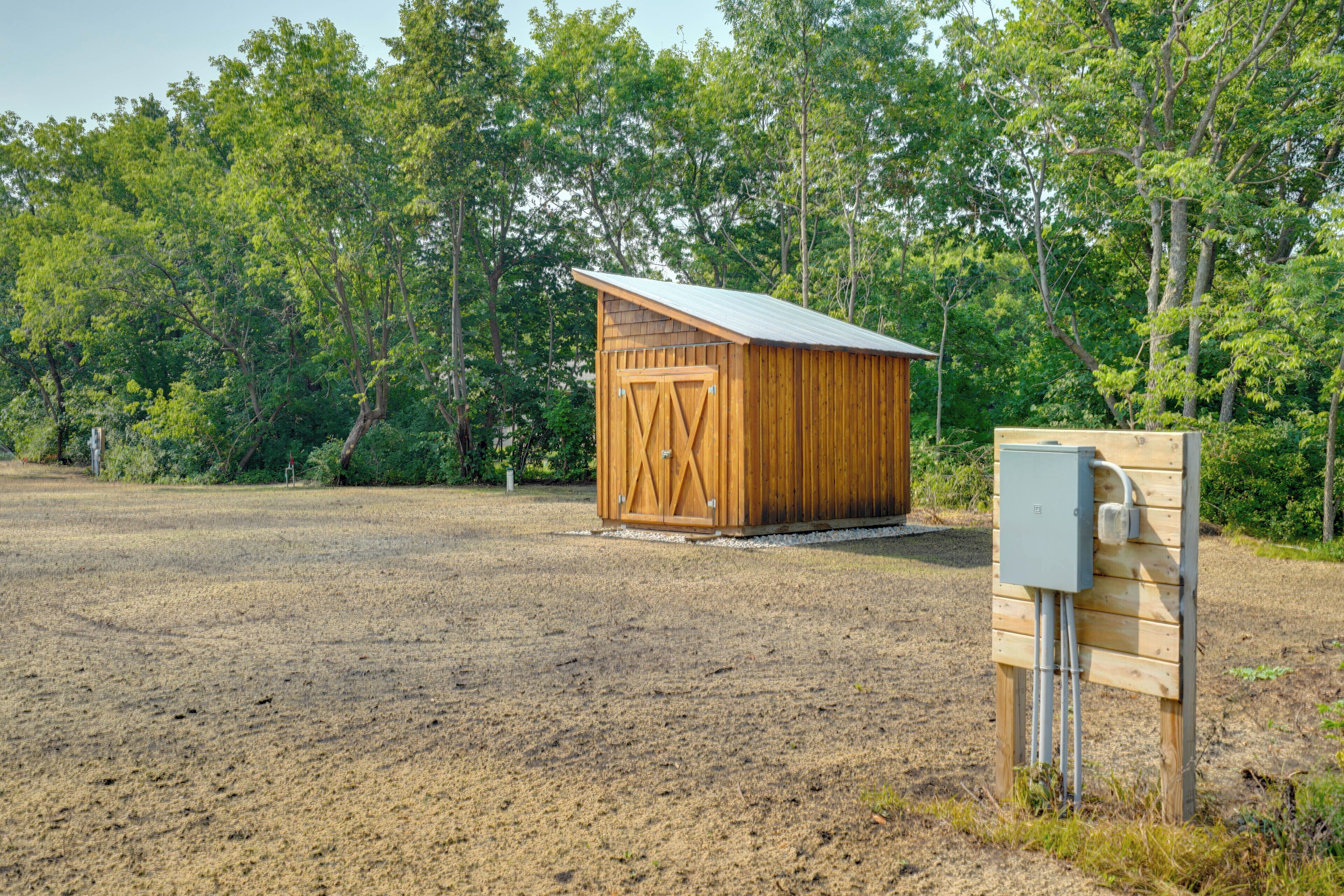 A wooden shed with a metal roof in a grassy field, surrounded by trees.
