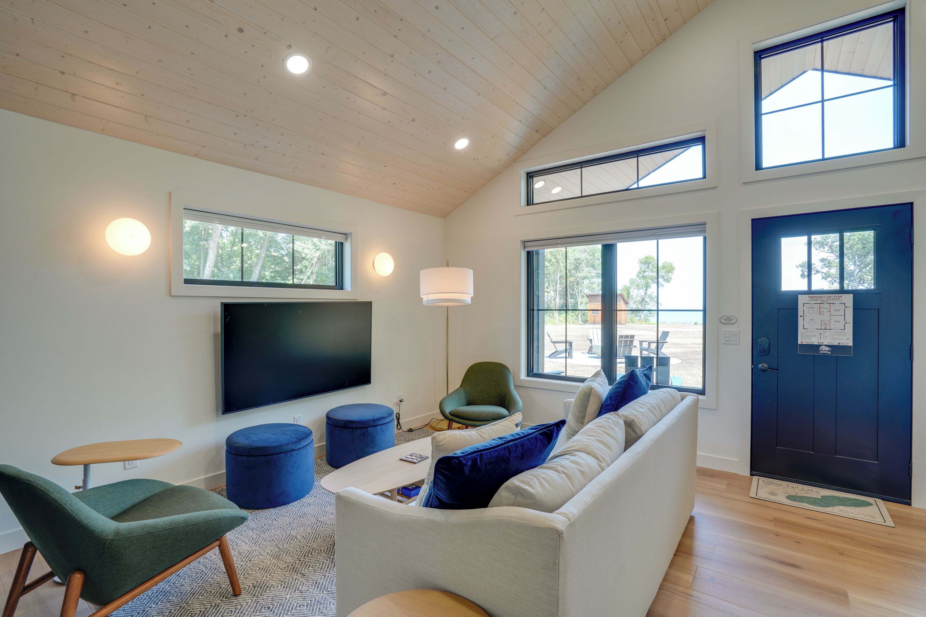 A modern living room with a flat-screen TV, comfortable seating, and large windows.