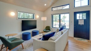A modern living room with a flat-screen TV, comfortable seating, and large windows.