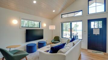A modern living room with a flat-screen TV, comfortable seating, and large windows.