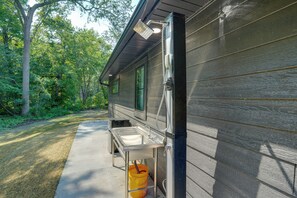 A cabin with a concrete pathway leading to a metal-framed outdoor sink and a yellow bucket.