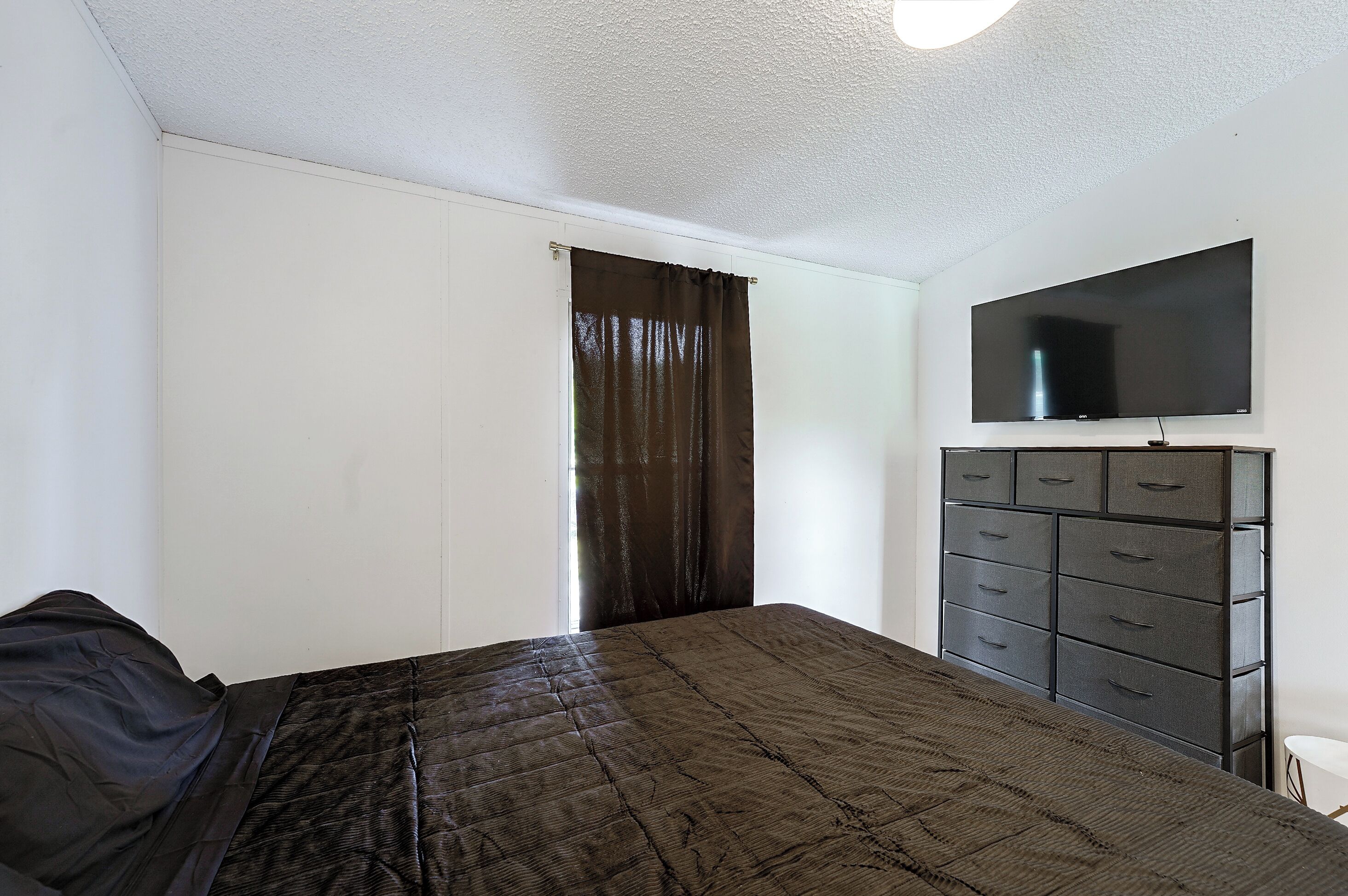 A bedroom with a bed, a dresser, and a television on the wall.