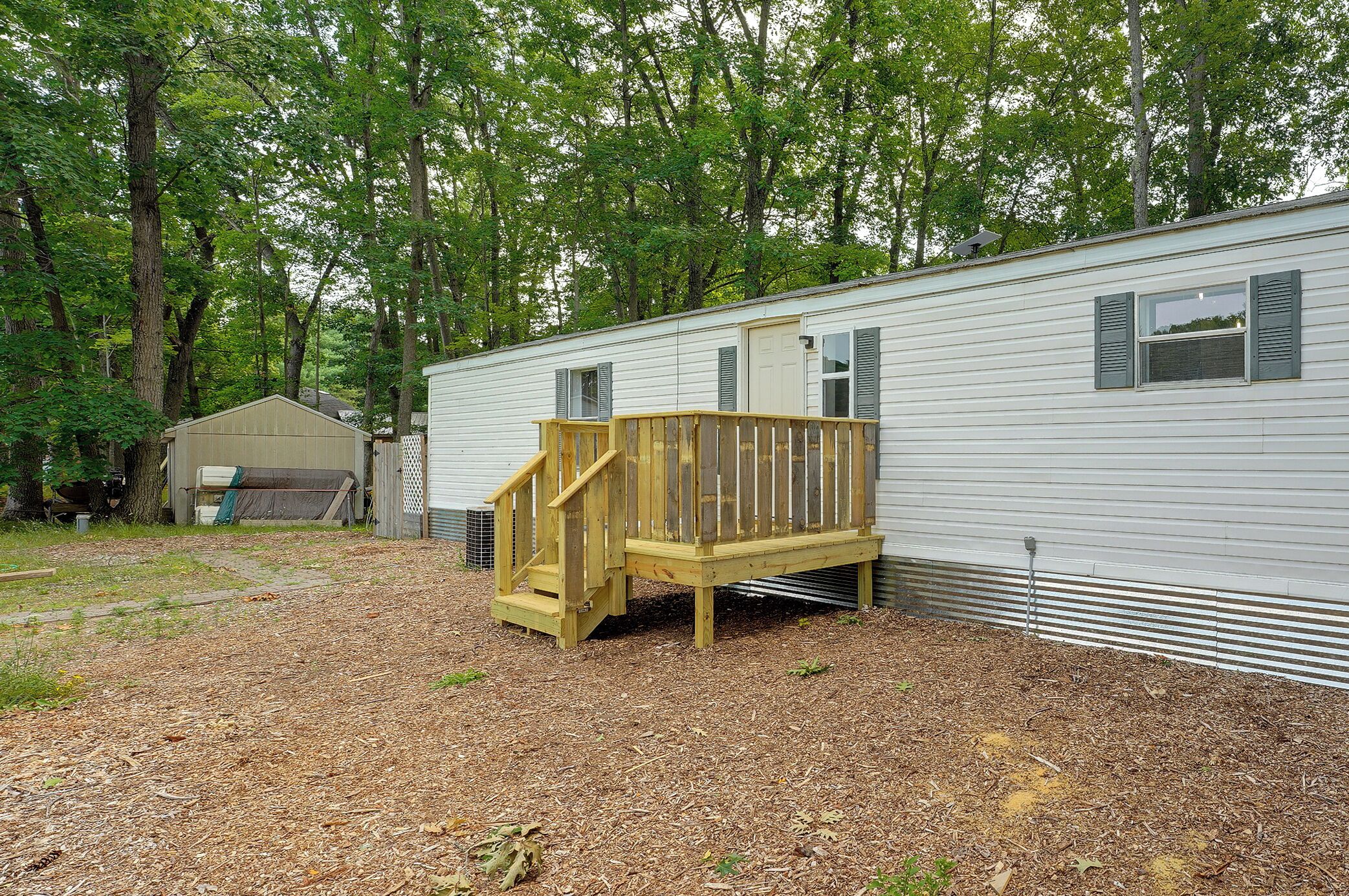 A mobile home with a wooden deck and a small staircase leading to a door.