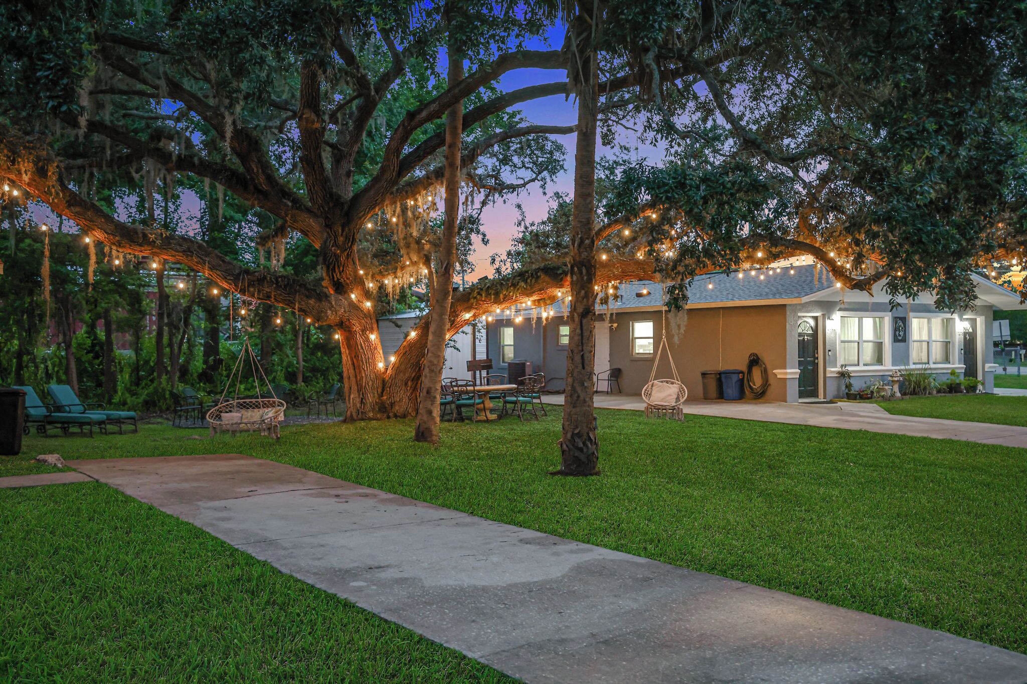 A well-maintained outdoor area with a pathway leading to a building, surrounded by trees and string lights.