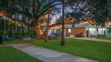 A well-maintained outdoor area with a pathway leading to a building, surrounded by trees and string lights.