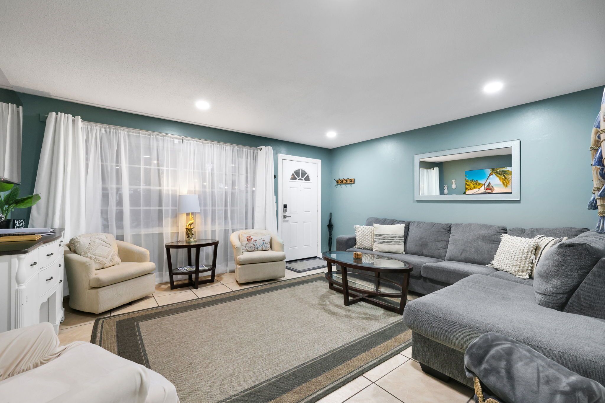 A living room with a grey sofa, two armchairs, a coffee table, and a TV on the wall.