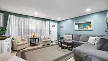 A living room with a grey sofa, two armchairs, a coffee table, and a TV on the wall.