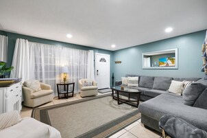A living room with a grey sofa, two armchairs, a coffee table, and a TV on the wall.