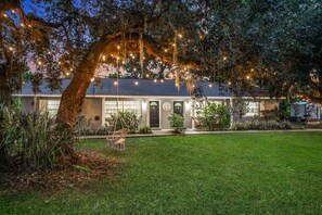 Uma casa com um amplo jardim frontal, uma cadeira balanço e luzes de cordão.