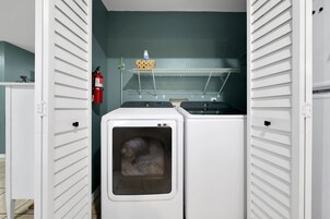 A laundry room with two dryers, a shelf with a basket and a bottle, and a fire extinguisher.